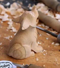 a wooden dog sitting on top of a table next to a knife and some wood shavings