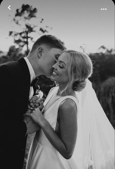 a bride and groom kissing in front of trees