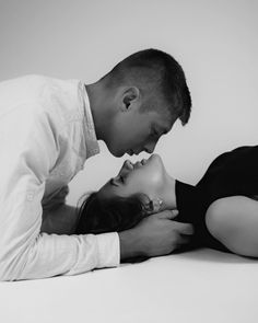 a man and woman laying on the ground kissing each other with their noses close together