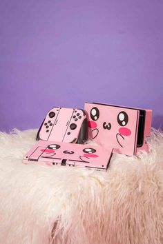 two pink nintendo wii game controllers sitting on top of a fluffy white blanket next to a purple wall