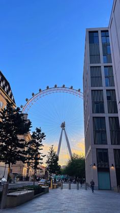 the london eye at dusk, with people walking on the sidewalk and buildings in the background