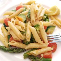 a white plate topped with pasta and veggies next to a slice of lemon