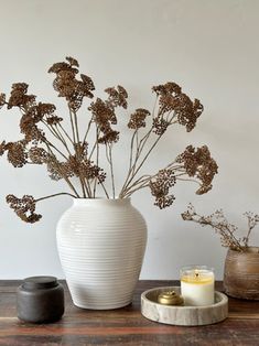 a white vase sitting on top of a wooden table next to a candle and some plants