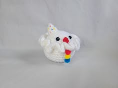 a crocheted white cupcake with a rainbow colored candy in it's mouth