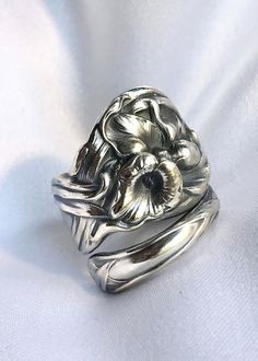 a silver ring with flowers on it sitting on top of a white cloth covered surface