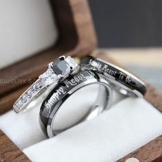 two wedding rings with names engraved on them sitting in a wooden ring box next to each other