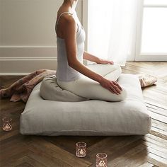 a woman sitting on a pillow in the middle of a room with candles around her