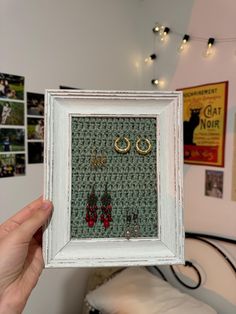 a person holding up a frame with earrings on it