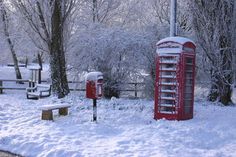 a red phone booth sitting in the middle of a snow covered park with benches and trees