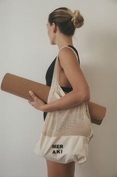 a woman carrying a yoga mat in her right hand and a tote bag with the word mer art printed on it