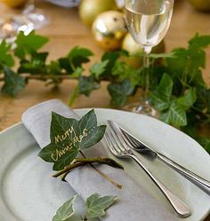 a white plate topped with a leaf next to a glass filled with wine and silverware