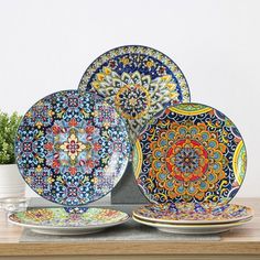 four colorful plates sitting on top of a wooden table next to a potted plant