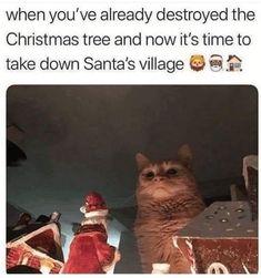 a cat sitting on top of a table next to a pile of christmas presents and santa's hat