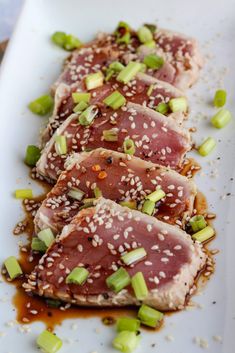 three pieces of meat on a white plate with sesame seeds and green onions sprinkled around it