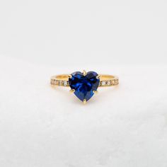 a heart shaped blue sapphire and diamond ring on top of snow covered ground with white background