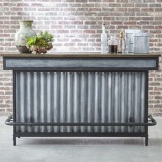 an old fashioned metal bar in front of a brick wall with a plant on top