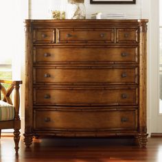 a wooden dresser sitting next to a window in a living room with a chair and painting on the wall