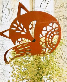 a vase filled with white flowers next to a red metal cat decoration on top of a table