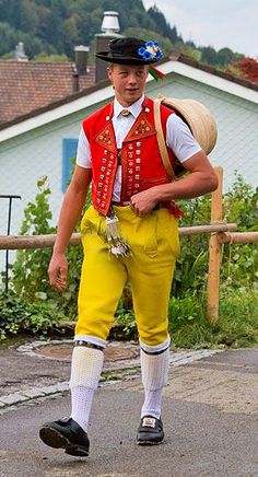 a man wearing yellow pants and a red vest is walking down the street with a hat on his head