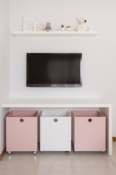 a flat screen tv mounted on top of a white wall next to pink and white drawers