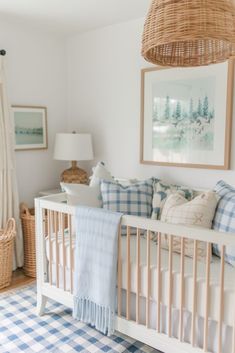 a baby's crib with blue and white checkered bedding, plaid pillows, and a wicker basket hanging from the ceiling