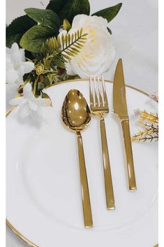 a white plate topped with gold flatware and flowers