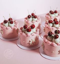 several small cakes with cherries and whipped cream on pink paper, sitting on plates