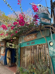 the front of a surf shop with flowers growing on it