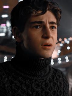 a close up of a person wearing a sweater and looking at the camera with city lights in the background