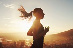 a woman running in the sun with her hair blowing in the wind while looking out over a city