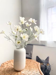 a white vase filled with flowers sitting on top of a table next to a black cat