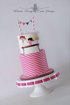 a pink and white striped cake with two people on top is sitting on a pedestal