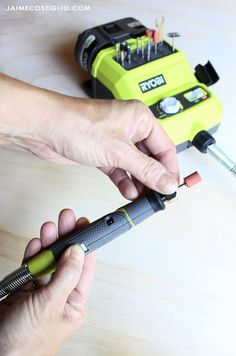 a person holding a green and black tool on top of a wooden table next to an electric screwdriver