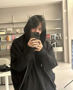 a man in a black hoodie taking a selfie with his cell phone while standing in front of a bookshelf