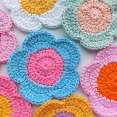 several crocheted flowers are arranged on a white surface with pink, yellow, and blue petals