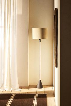 a floor lamp sitting in front of a window next to a white curtained wall