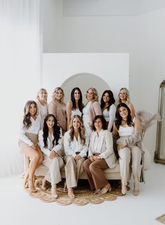 a group of women sitting next to each other in front of a white wall with a mirror