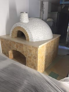 an outdoor brick pizza oven on top of a wooden table next to a white wall