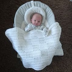 a baby in a crocheted blanket laying on the floor