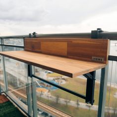 a wooden bench sitting on top of a metal and glass balcony next to a green field