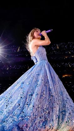 a woman in a blue dress holding a microphone and singing into the air at night