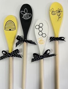 four wooden spoons decorated with bees and honeycombs are lined up against a white wall