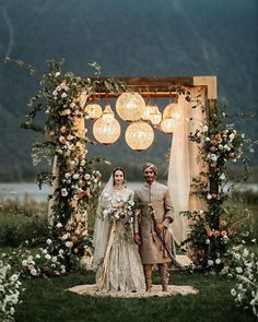 a man and woman standing in front of a wedding arch with flowers on the side