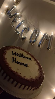 a welcome home cake with frosting on it and lights in the backround