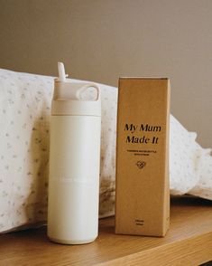 thermos bottle is next to an empty box on a wooden shelf in front of a bed