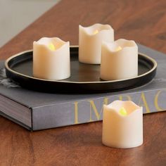 four white candles sitting on top of a book