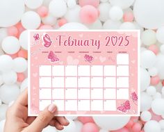 a person holding up a calendar with pink butterflies on it and balloons in the background