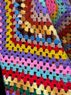 a multicolored crocheted blanket is laying on a black surface