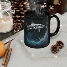 a coffee mug with a shark on it sitting next to some pine cones and candles