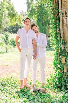 two young men standing next to each other in front of a tree and ivy covered wall